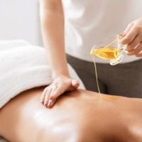 Spa treatment. Masseur pouring aroma oil on female back, doing massage